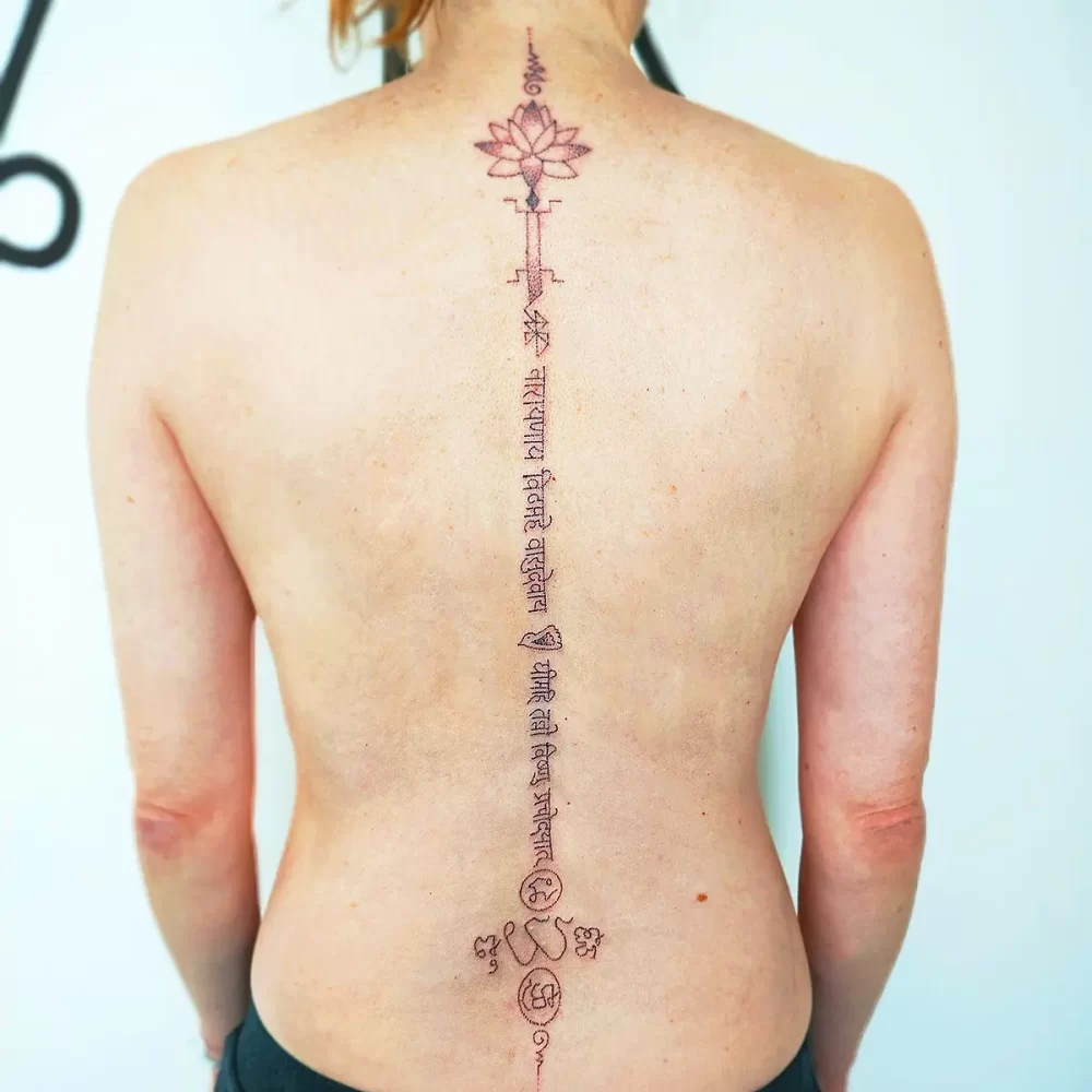 Tatouage spirituel colonne vertébrale – mantra sacré et lotus pour réalignement énergétique Tatouage spirituel le long de la colonne vertébrale avec mantra sanskrit et lotus sacré, réalisé à la main