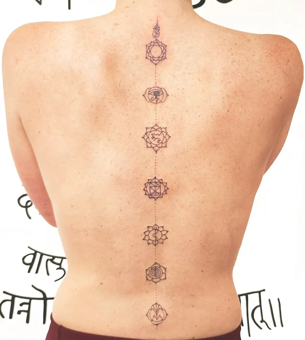 Tatouage spirituel handpoke le long de la colonne vertébrale, représentant l’alignement des chakras Tatouage handpoke des chakras alignés sur la colonne vertébrale d’une femme