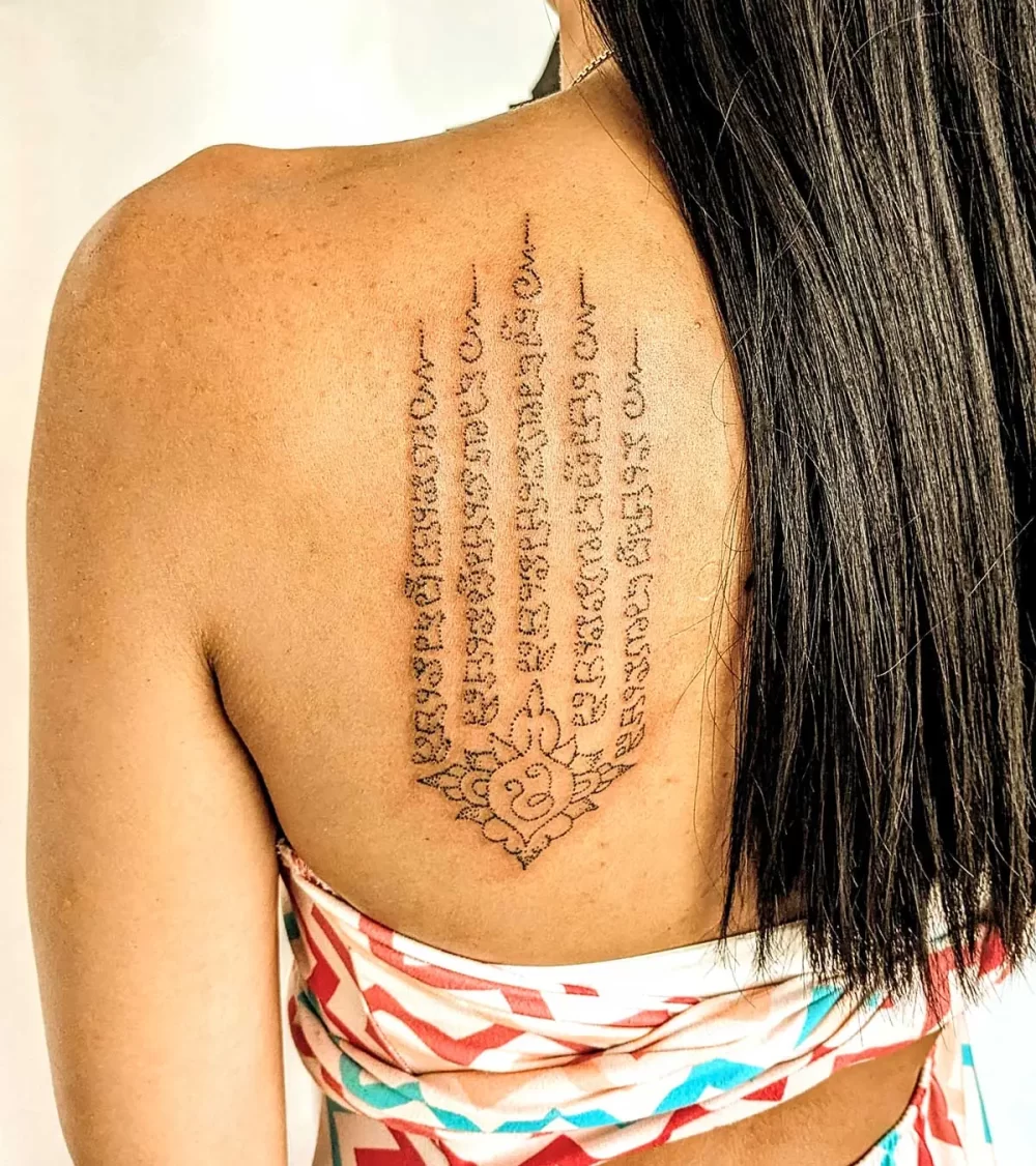 Hah Taew cinq lignes avec lotus, omoplate, réalisé au handpoke sur peau mate
